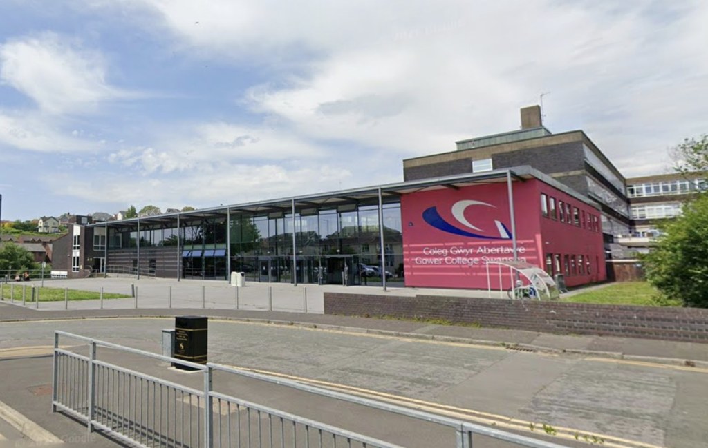 The glass-fronted main entrance of Gower College Swansea's Tycoch campus with its red Coleg Gwyr Abertawe sign, and the older brick tower block behind