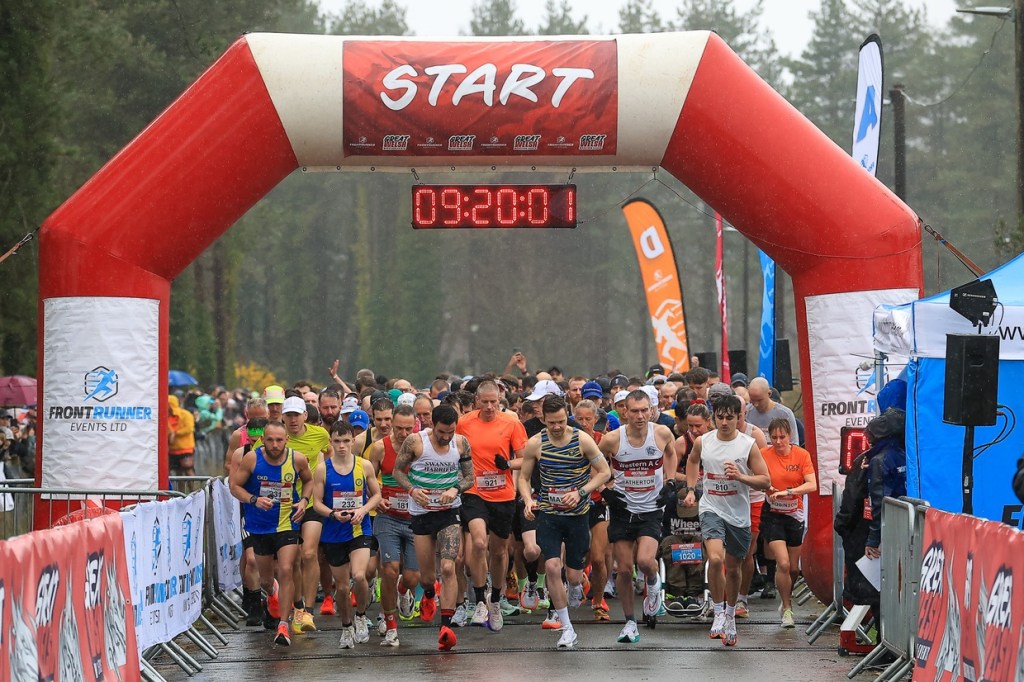 Runners setting off beneath a red inflatable start arch in the rain at the Great Welsh Marathon at Pembrey Country Park