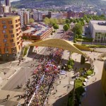 Aerial view of thousands of runners gathered at a start arch beneath the golden Copr Bay bridge in Swansea city centre