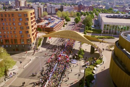 Aerial view of thousands of runners gathered at a start arch beneath the golden Copr Bay bridge in Swansea city centre