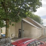 The single-storey surgery building in Gwaun Cae Gurwen, partly hidden behind a large tree, with cars parked outside