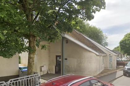 The single-storey surgery building in Gwaun Cae Gurwen, partly hidden behind a large tree, with cars parked outside