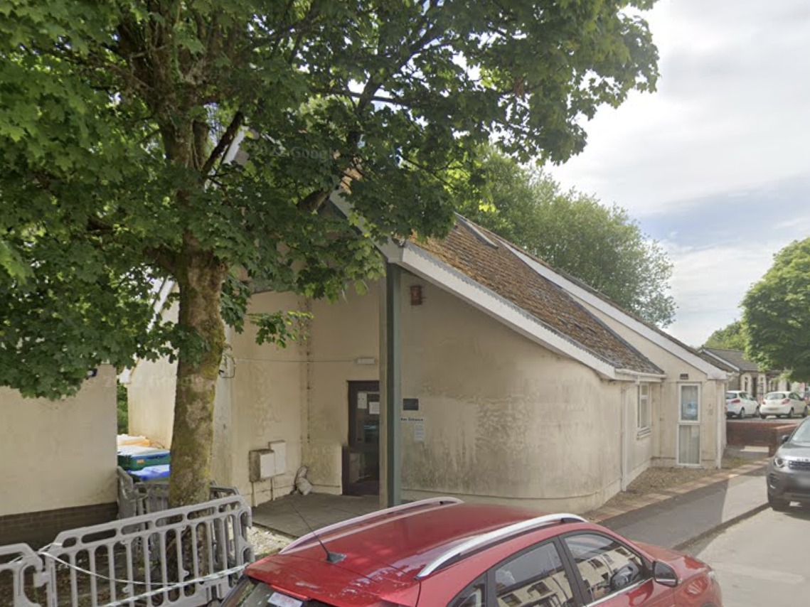 The single-storey surgery building in Gwaun Cae Gurwen, partly hidden behind a large tree, with cars parked outside