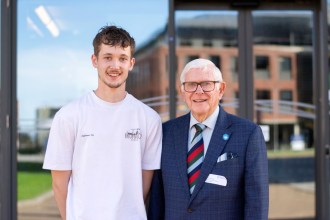 Freddie Williams, 19, in a white T-shirt beside his grandfather Handel Williams, 83, in a checked suit and striped tie, outside the engineering building at Swansea University's Bay Campus