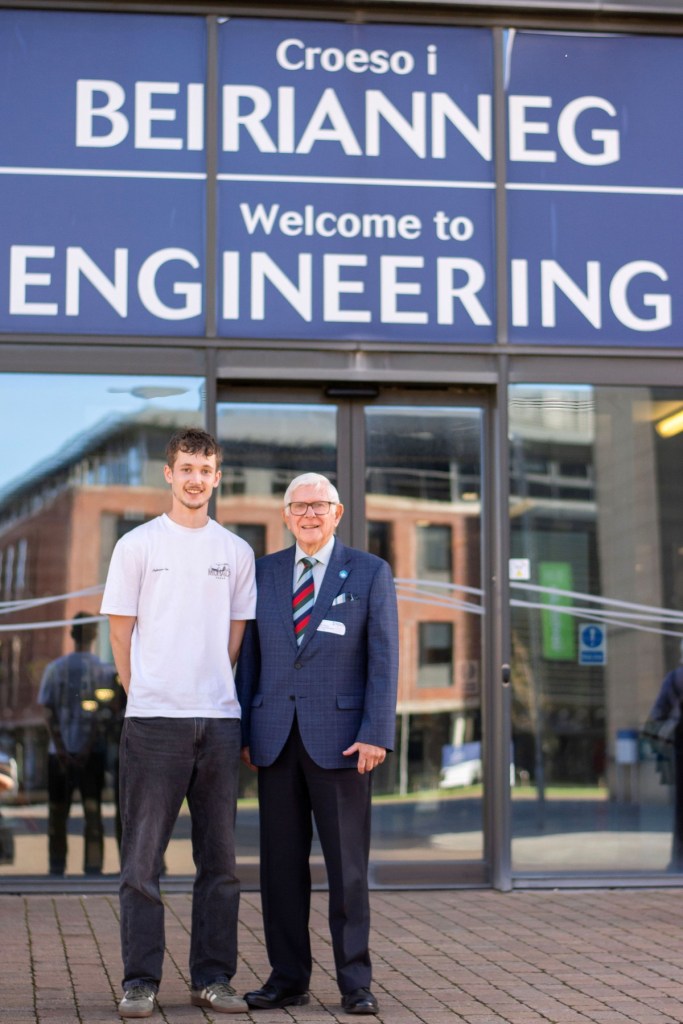 Freddie and Handel Williams standing under the bilingual Welcome to Engineering sign at Swansea University's Bay Campus