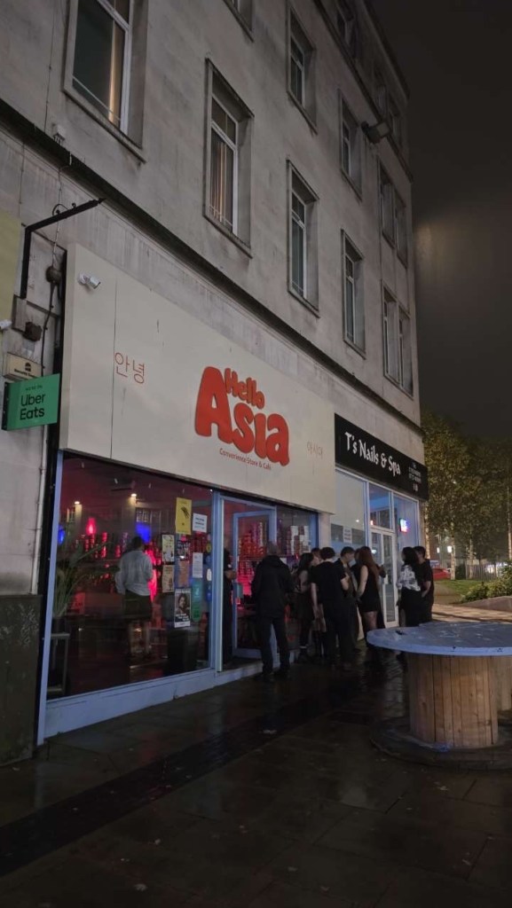 People queuing on the wet pavement outside Hello Asia convenience store on Princess Way, Swansea, at night for the LibertySounds club event