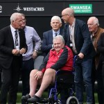 John Toshack, seated in a red and black jacket, surrounded by members of Swansea City's 1981 team pitchside at the Swansea.com Stadium