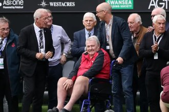 John Toshack, seated in a red and black jacket, surrounded by members of Swansea City's 1981 team pitchside at the Swansea.com Stadium