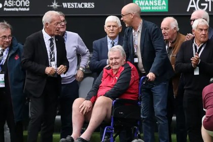 John Toshack, seated in a red and black jacket, surrounded by members of Swansea City's 1981 team pitchside at the Swansea.com Stadium