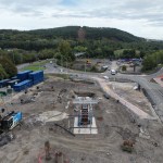 Drone view of the Skyline gondola base station site at Landore, with a piling rig, blue site cabins and a scaffolded column of steel reinforcement on a concrete base, and the cleared gondola line running up Kilvey Hill behind