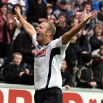 Lee Trundle in a white Swansea City shirt with both arms raised, celebrating in front of a packed stand