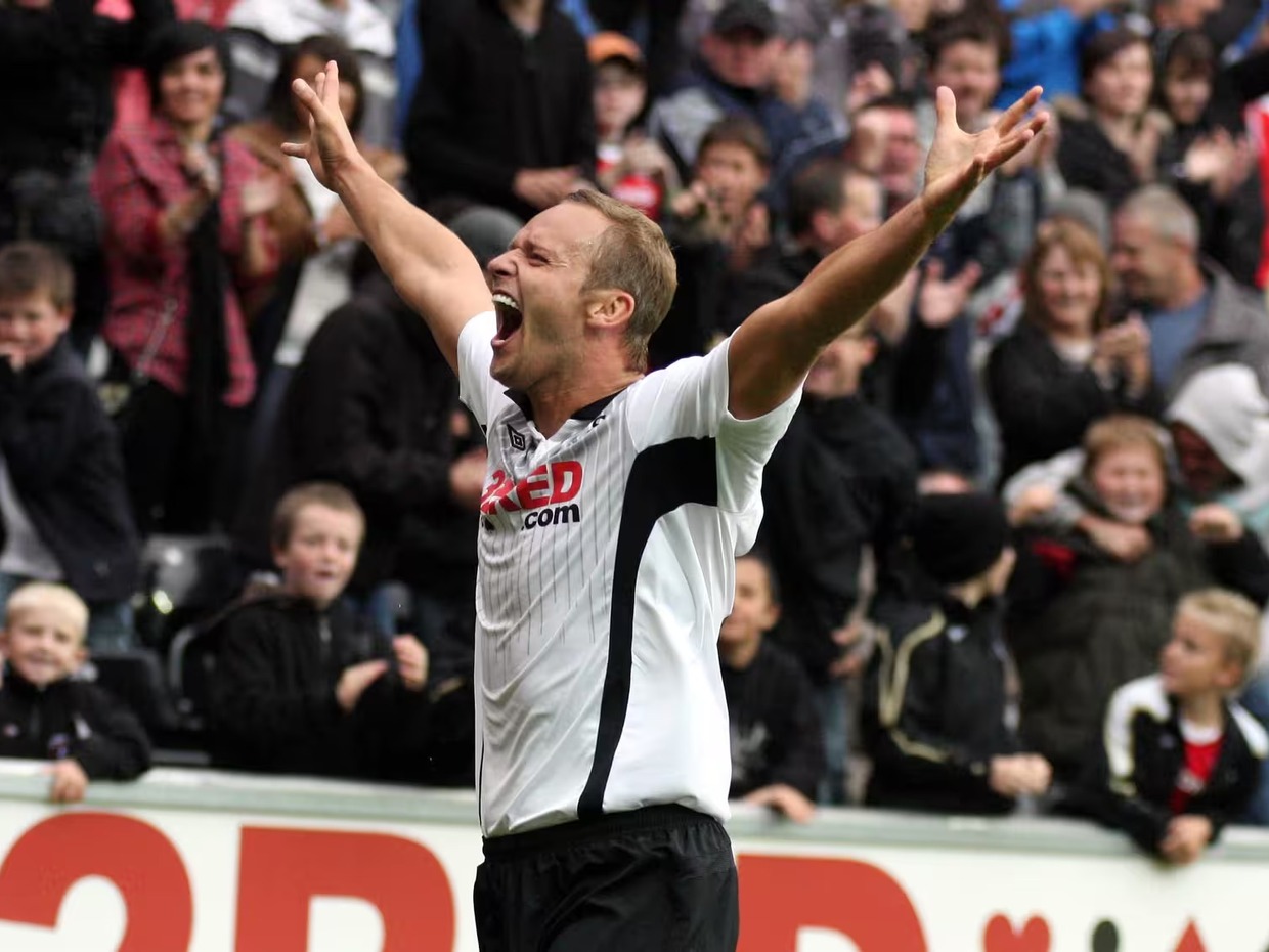 Lee Trundle in a white Swansea City shirt with both arms raised, celebrating in front of a packed stand