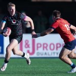 Lewis Edwards running with the ball in a black Wales kit as a defender in red closes in