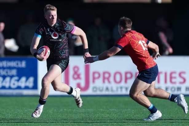 Lewis Edwards running with the ball in a black Wales kit as a defender in red closes in