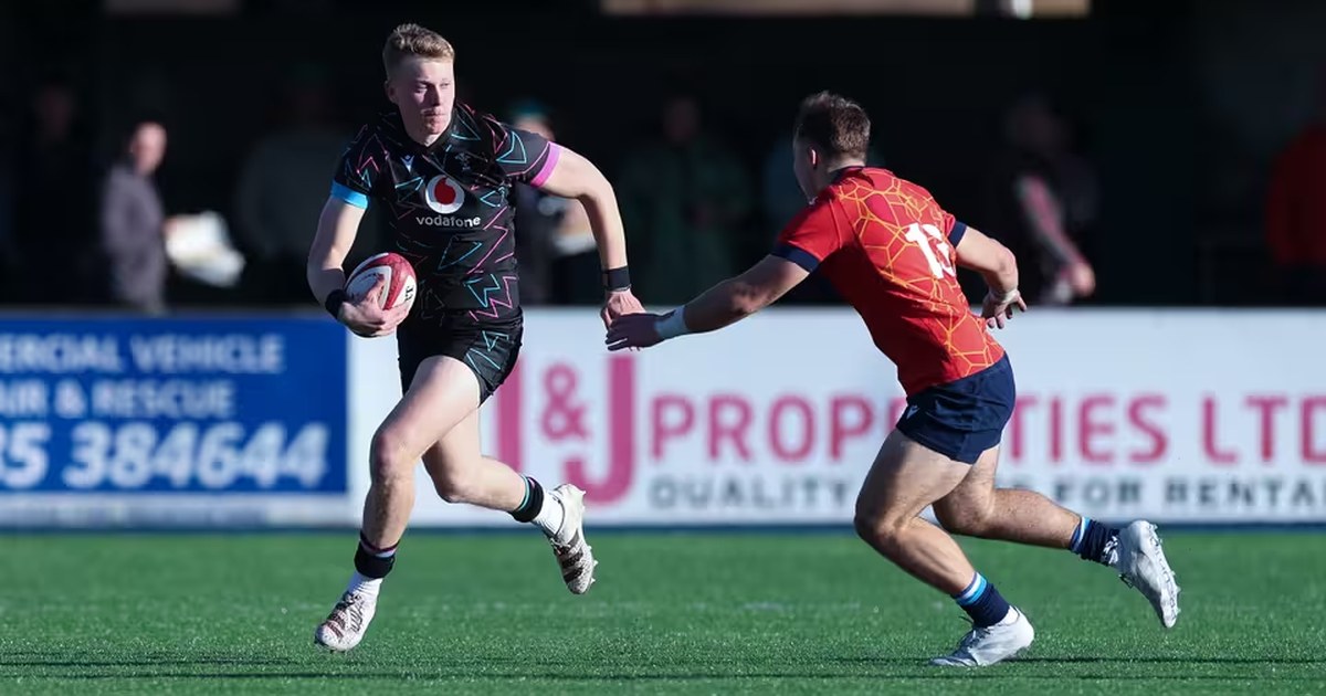 Lewis Edwards running with the ball in a black Wales kit as a defender in red closes in