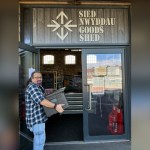 A volunteer carries a box of meals into the Goods Shed in Llanelli, under a sign reading Sied Nwyddau Goods Shed