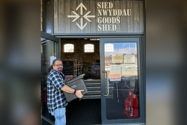 A volunteer carries a box of meals into the Goods Shed in Llanelli, under a sign reading Sied Nwyddau Goods Shed