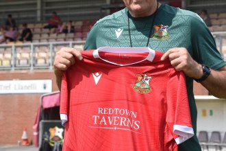 Terry Boyle in a green Llanelli Town training top holding up a red Llanelli Town home shirt at Stebonheath Park