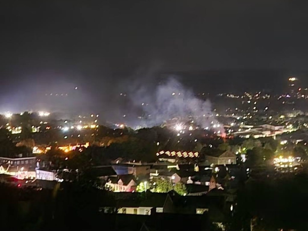 Grey smoke drifting over the lights of Llansamlet at night, with a small orange glow of flame near Pant y Blawd