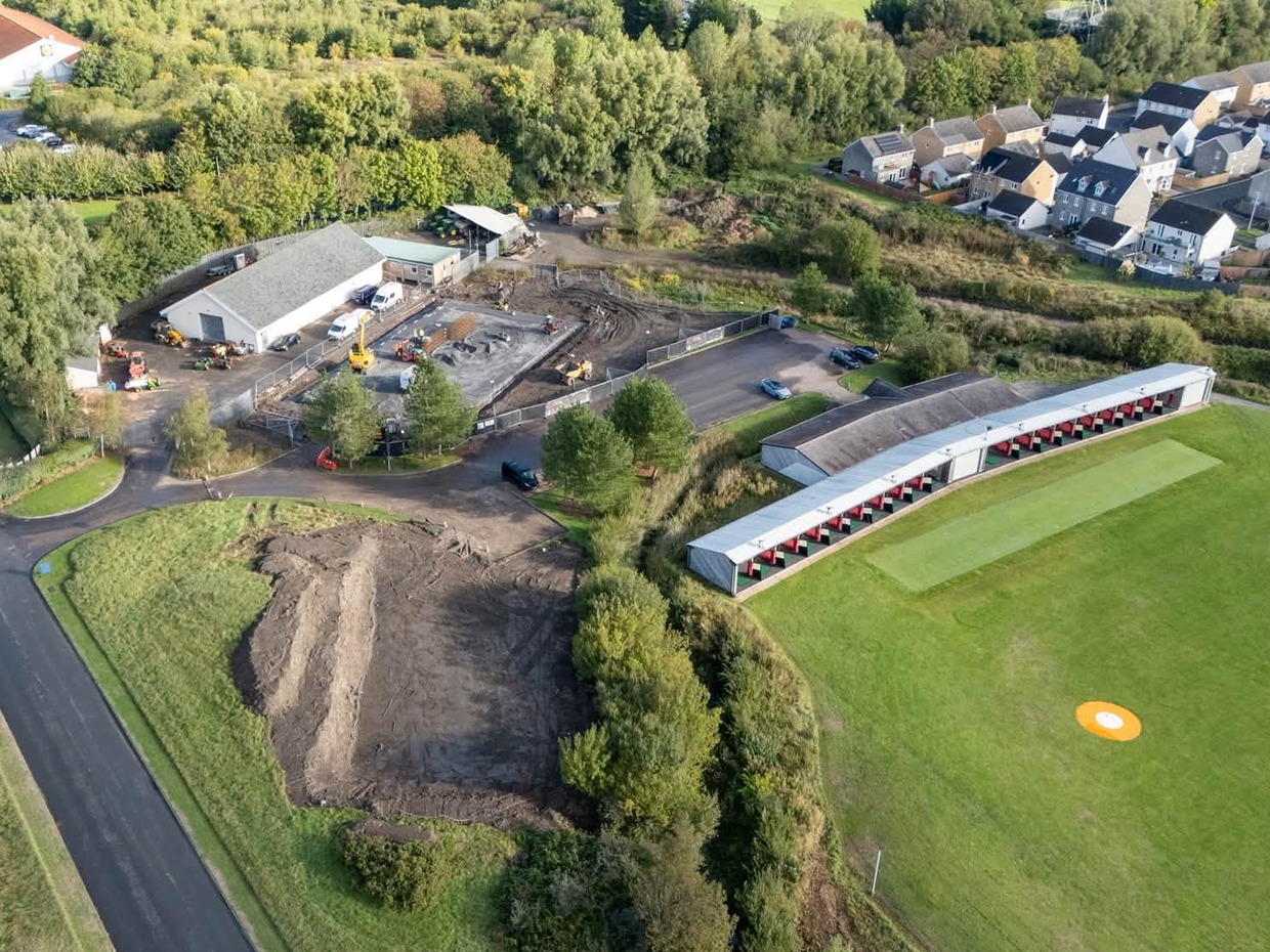 Aerial view of the Machynys golf club driving range, with a fenced building site and concrete slab beside the club's maintenance shed, and houses beyond