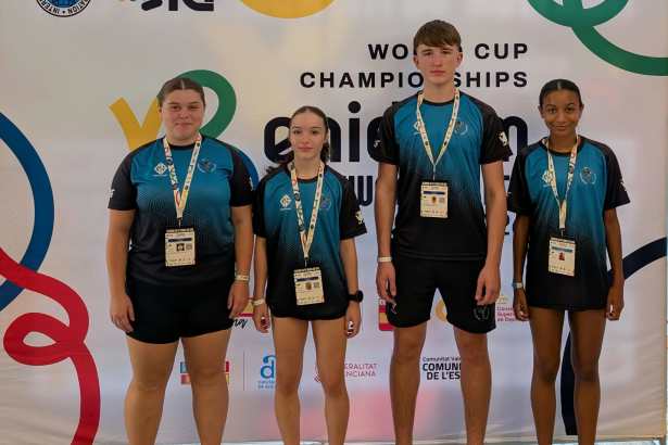 Four young taekwon-do athletes in matching teal and black club shirts stand in front of the ITF Taekwon-Do World Cup board in Benidorm