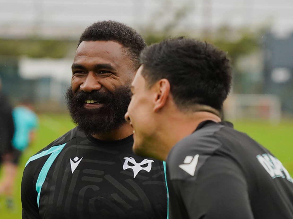 Ospreys wing Marika Koroibete, bearded and smiling, in a black Ospreys training top as a team-mate laughs beside him