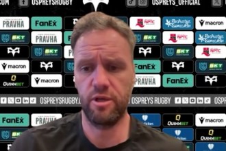 Ospreys head coach Mark Jones speaking at a press conference in front of a sponsor board