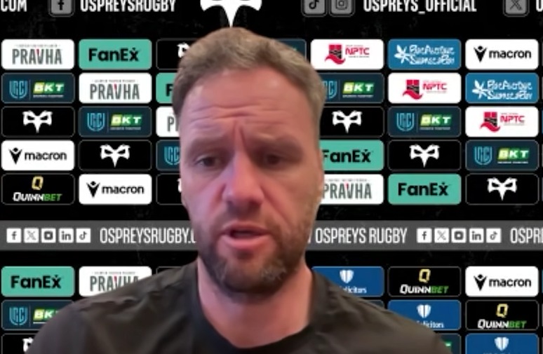 Ospreys head coach Mark Jones speaking at a press conference in front of a sponsor board