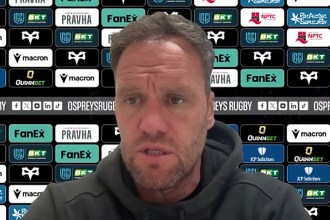 Ospreys head coach Mark Jones speaking at a press conference in front of a sponsor board