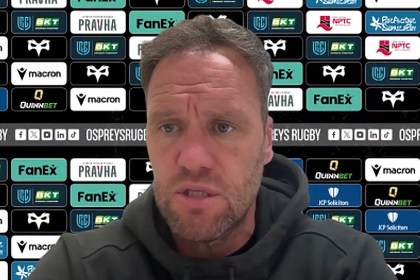 Ospreys head coach Mark Jones speaking at a press conference in front of a sponsor board