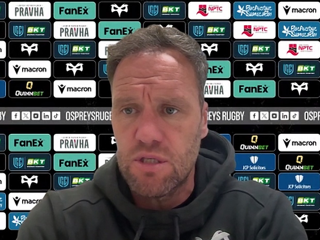 Ospreys head coach Mark Jones speaking at a press conference in front of a sponsor board