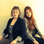 Mary Hopkin and her daughter Jessica Lee Morgan sitting back to back against a plain wall