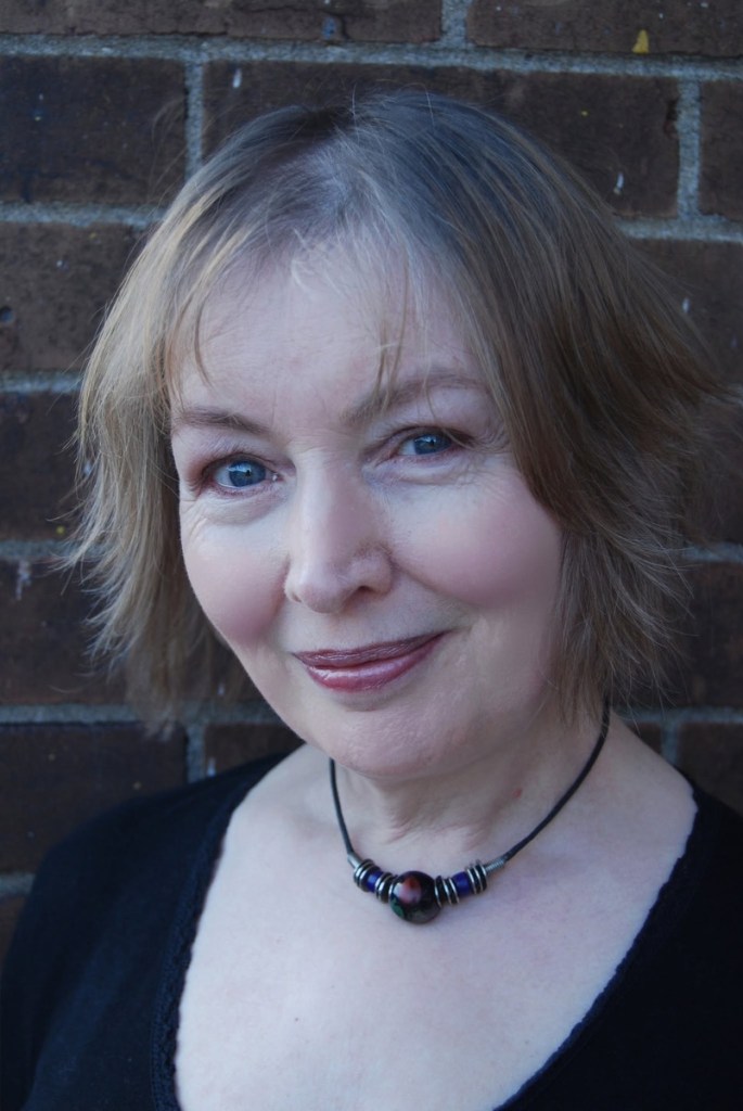 Mary Hopkin smiling in front of a brick wall
