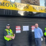 Swansea Council's lead trading standards officer Rhys Harries with two South Wales Police officers in front of the closed shutters of Monsoon Vape in Morriston, with court closure notices displayed