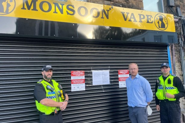 Swansea Council's lead trading standards officer Rhys Harries with two South Wales Police officers in front of the closed shutters of Monsoon Vape in Morriston, with court closure notices displayed