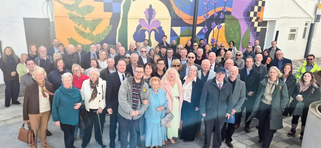 A group of guests stand in front of the Rewilding the City mural at Mowbray Yard, Swansea