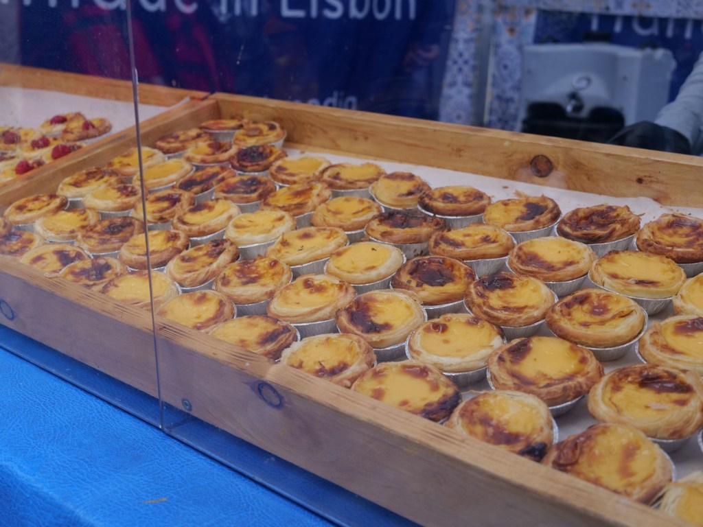 Trays of Portuguese custard tarts under a clear counter guard on a festival stall