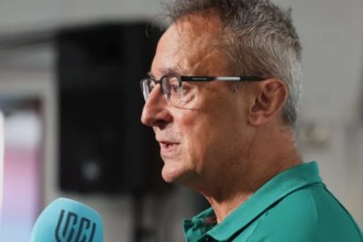 Scarlets director of rugby Nigel Davies in a green club polo shirt and glasses, speaking into a URC microphone