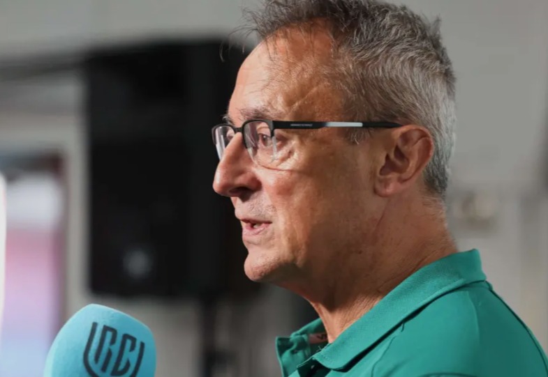Scarlets director of rugby Nigel Davies in a green club polo shirt and glasses, speaking into a URC microphone