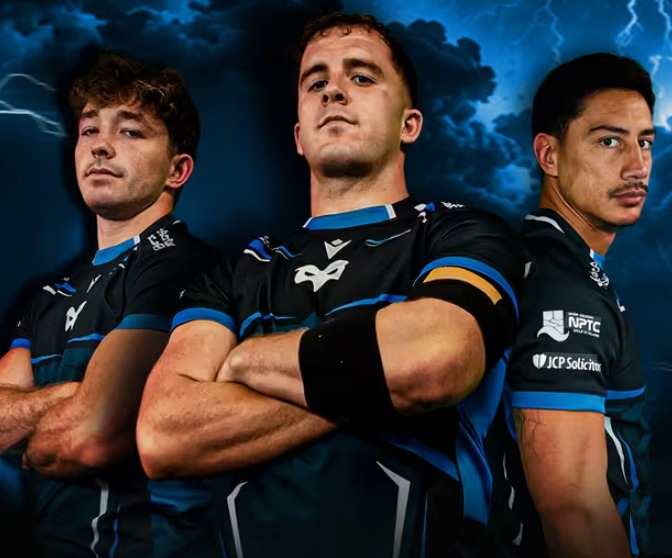 Three Ospreys players with arms folded in the dark blue and silver 2026/27 European kit against a stormy sky