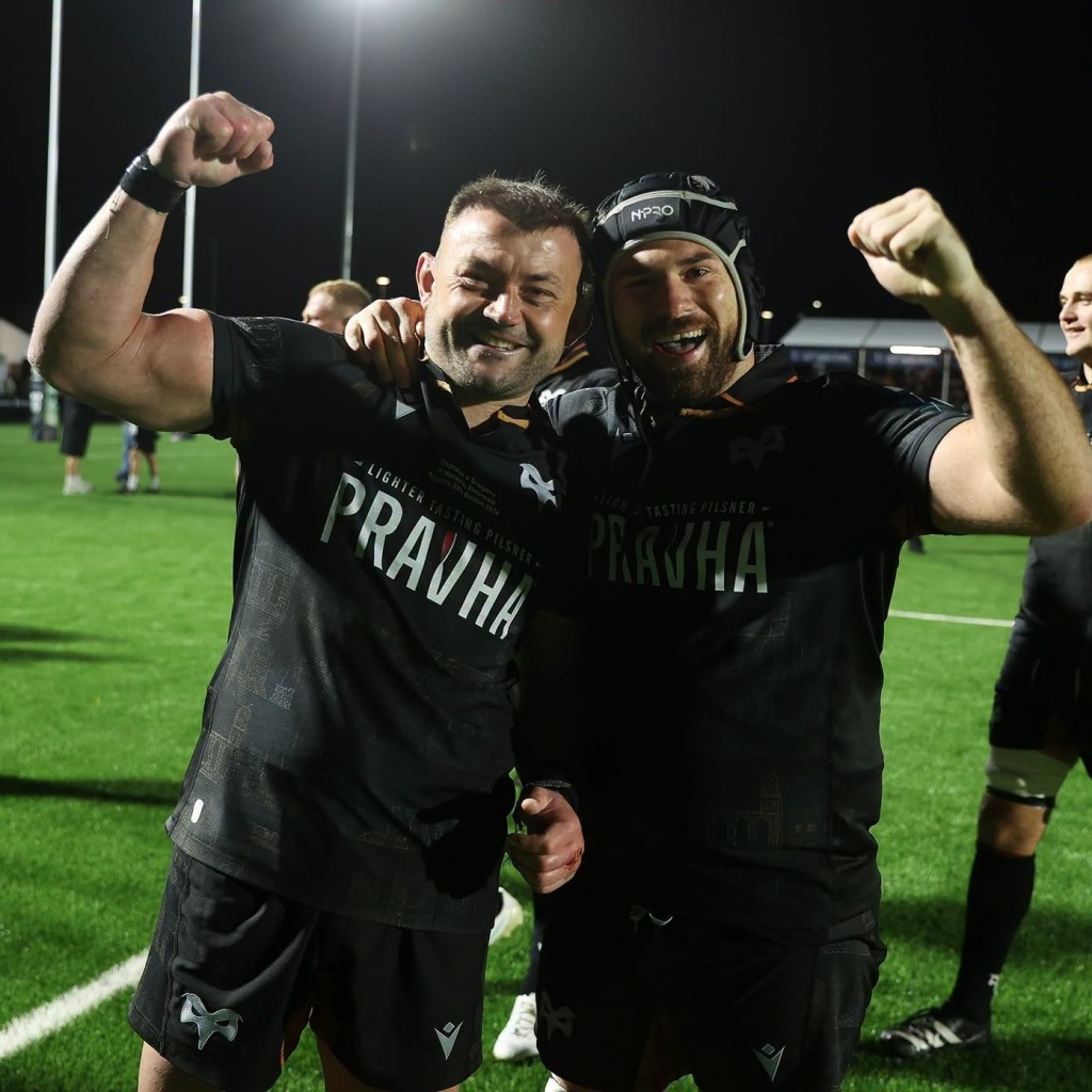 Two Ospreys players raising their fists in celebration on the pitch after the final whistle