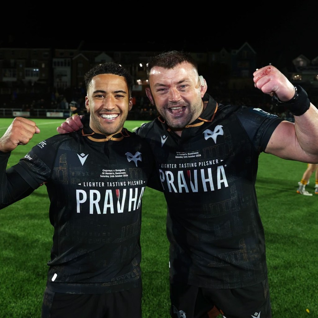 Two smiling Ospreys players with their arms round each other, fists raised, on the St Helen’s pitch