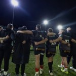 Ospreys players and staff in a huddle on the pitch under floodlights