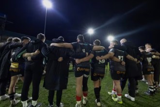 Ospreys players and staff in a huddle on the pitch under floodlights