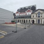 Temporary metal fencing across the empty lower section of Oxford Street car park in Swansea, with the Grand Theatre behind