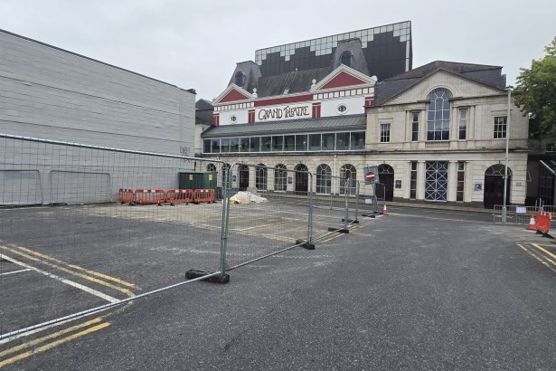 Temporary metal fencing across the empty lower section of Oxford Street car park in Swansea, with the Grand Theatre behind