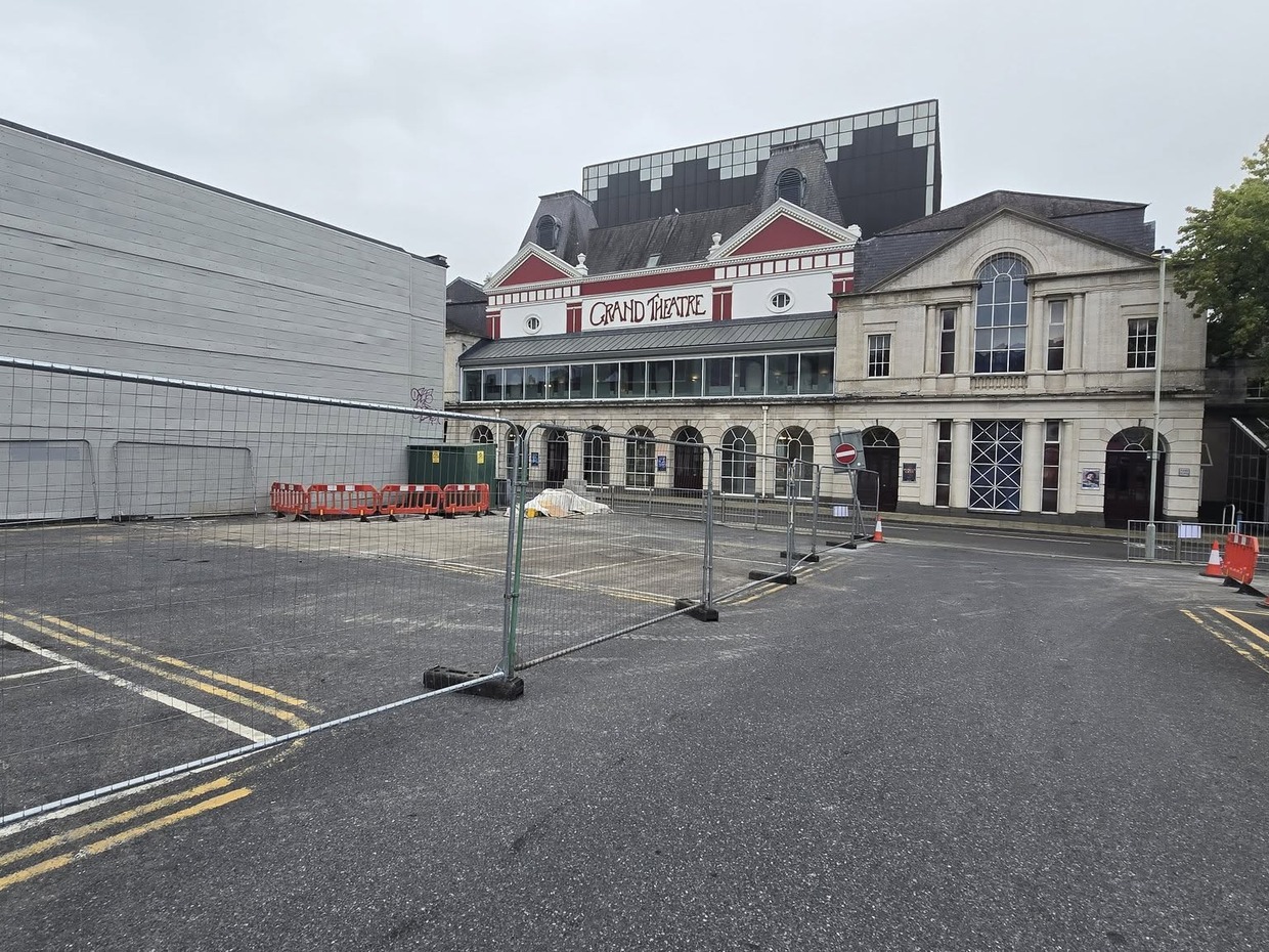 Temporary metal fencing across the empty lower section of Oxford Street car park in Swansea, with the Grand Theatre behind