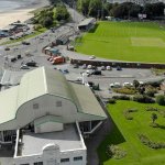 Aerial view of the Patti Pavilion with its curved green roof in Victoria Park, Swansea, with the St Helen's ground, Mumbles Road and the beach behind