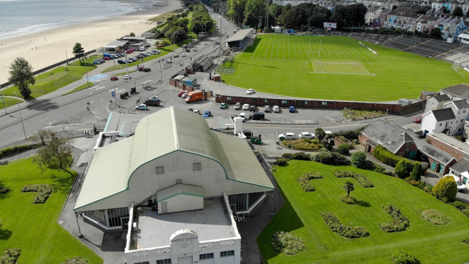 Aerial view of the Patti Pavilion with its curved green roof in Victoria Park, Swansea, with the St Helen's ground, Mumbles Road and the beach behind