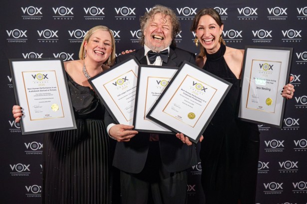 Nikki Mills, Phil Rowe and Jess Nesling laugh on the red carpet holding five framed VOX Awards certificates